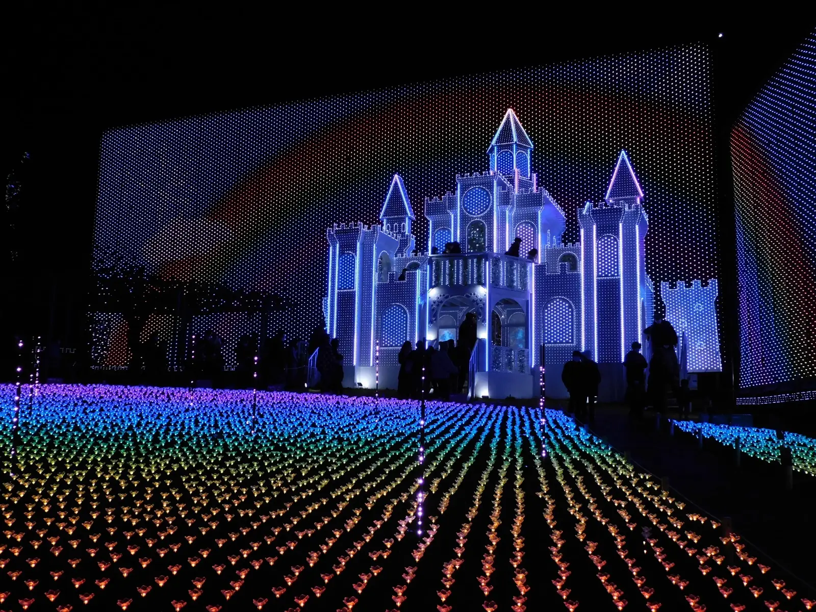 An illuminated castle and a field of rainbow lights at the Flower Fantasy illumination in Ashikaga Flower Park