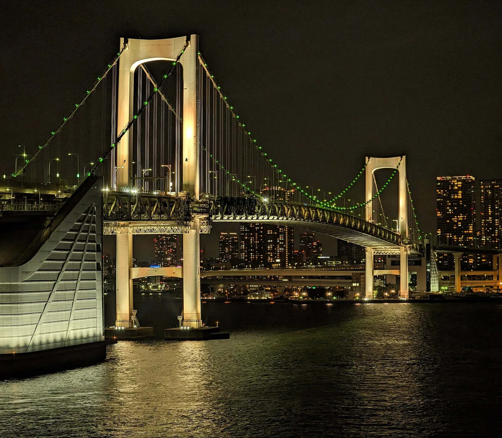 The Rainbow Bridge at night from the Odaiba side, the towers of the bay behind it