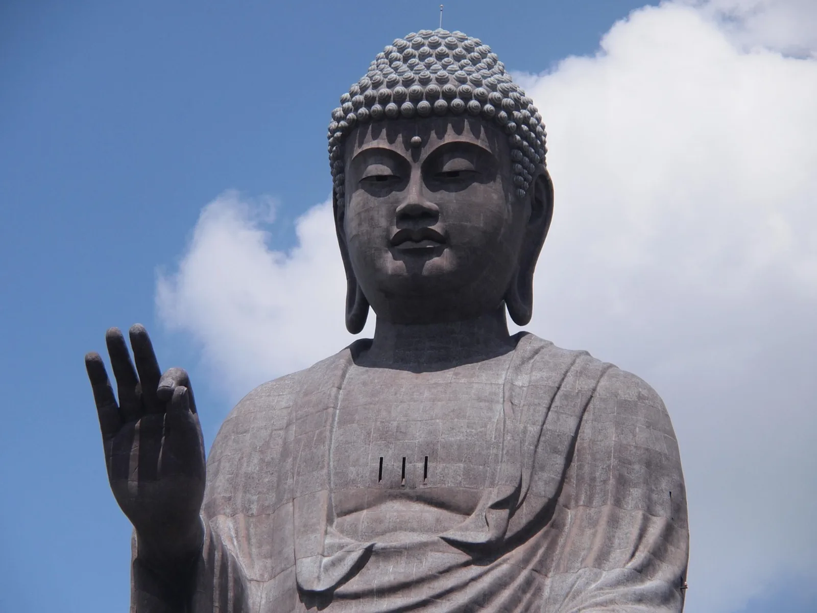 The upper body and raised hand of the bronze Ushiku Daibutsu against a blue sky